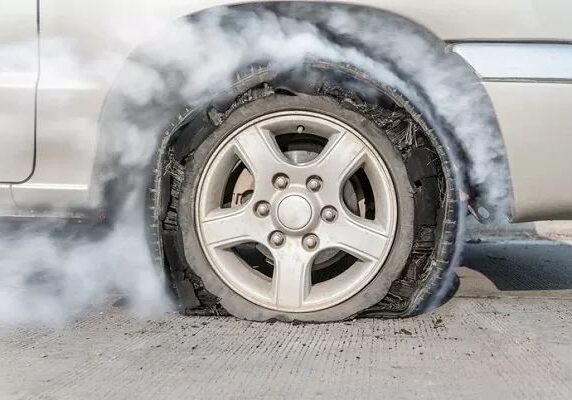 Car with smoking flat tire on pavement.