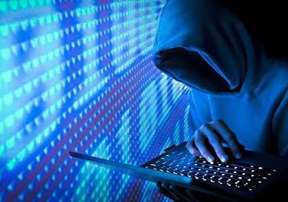 Hacker in hoodie using a laptop computer.