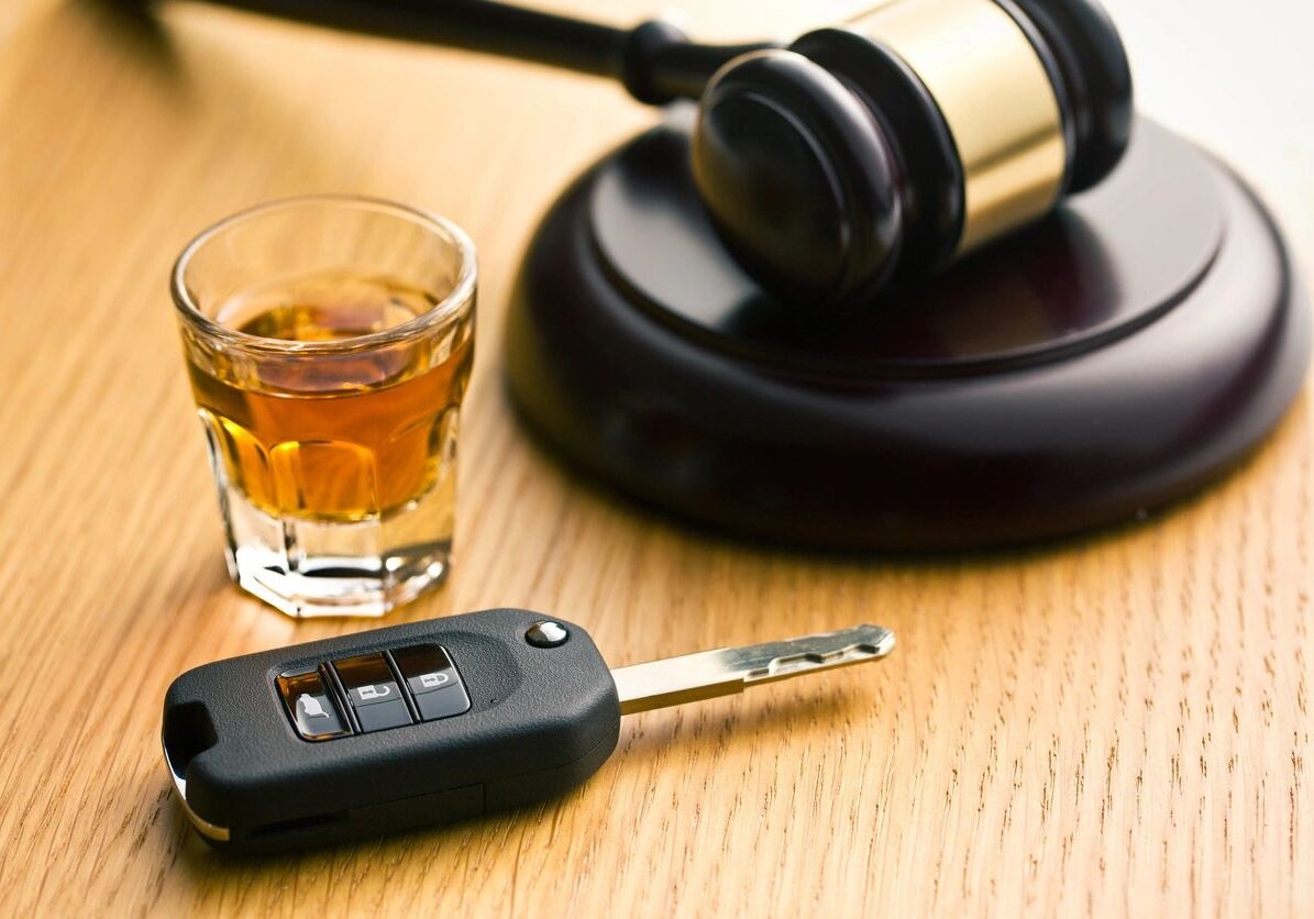 Gavel, car key, and whiskey on table.