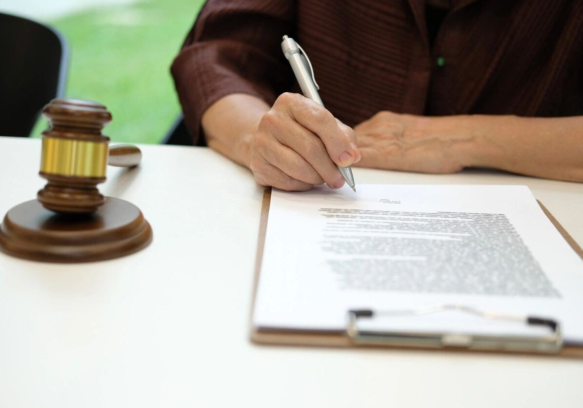 Hand signing document near gavel on desk.