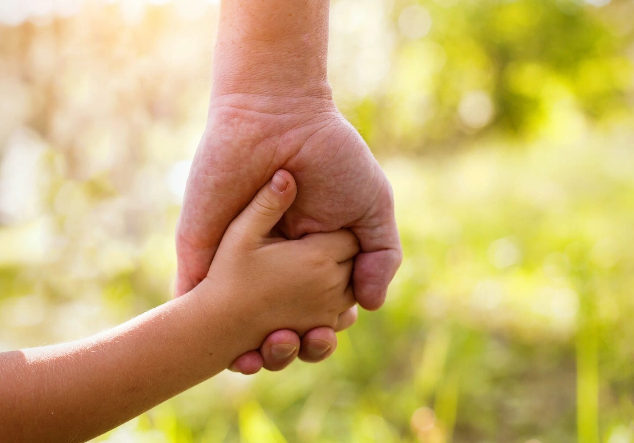 Adult and child holding hands outdoors.