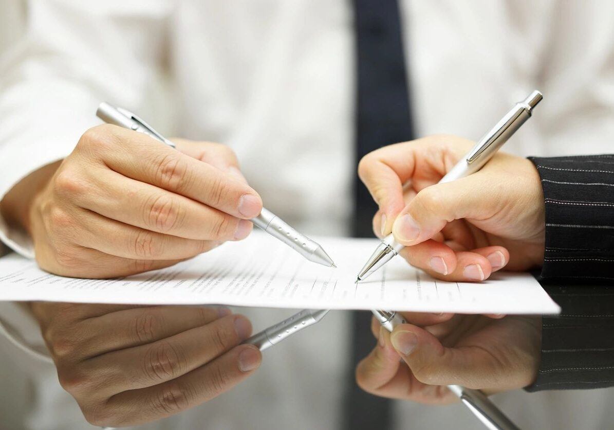 Hands signing a document with pens.