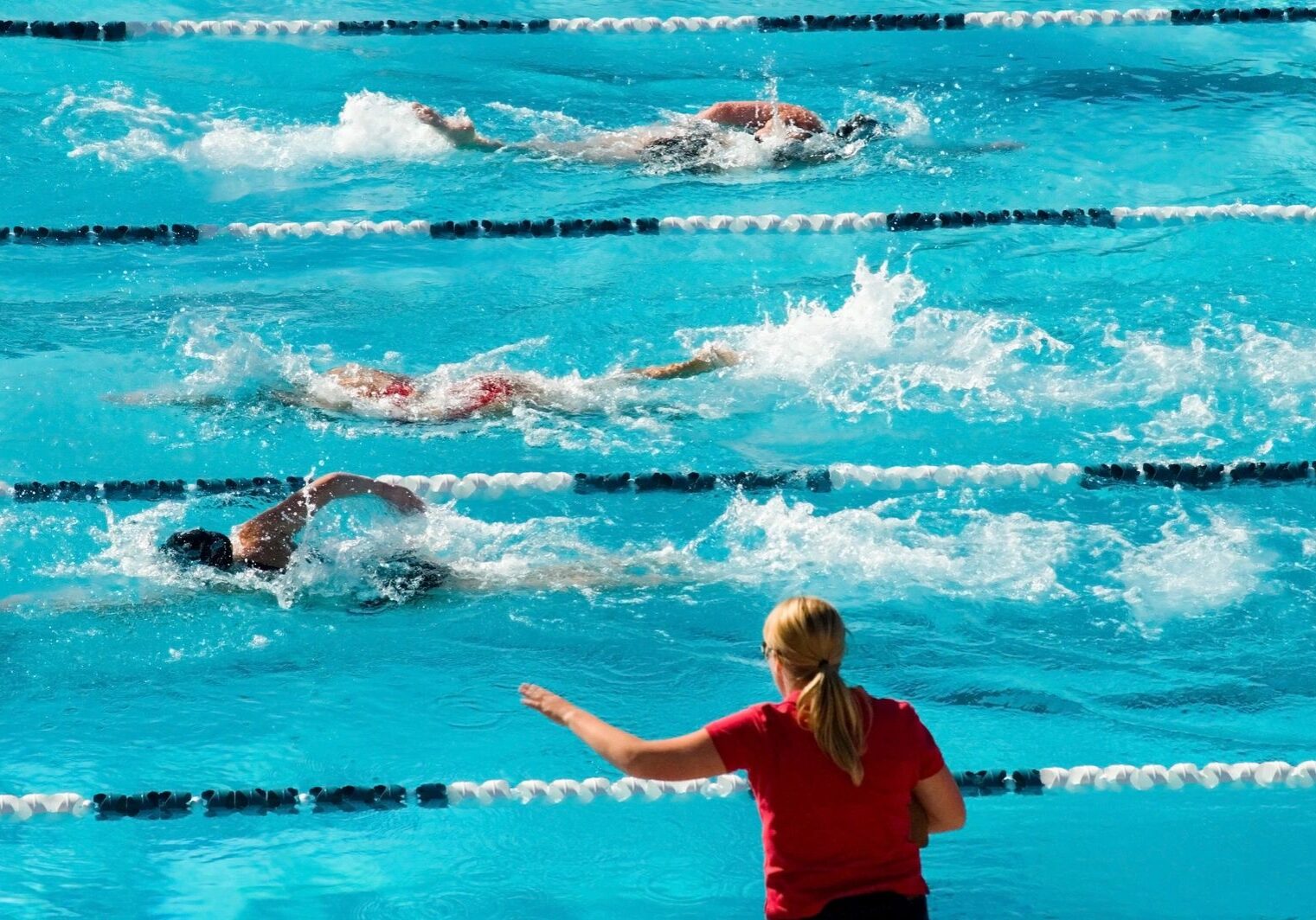 Swimmers racing in a pool, coach observing.