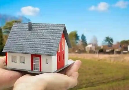 Hands holding miniature house in landscape.