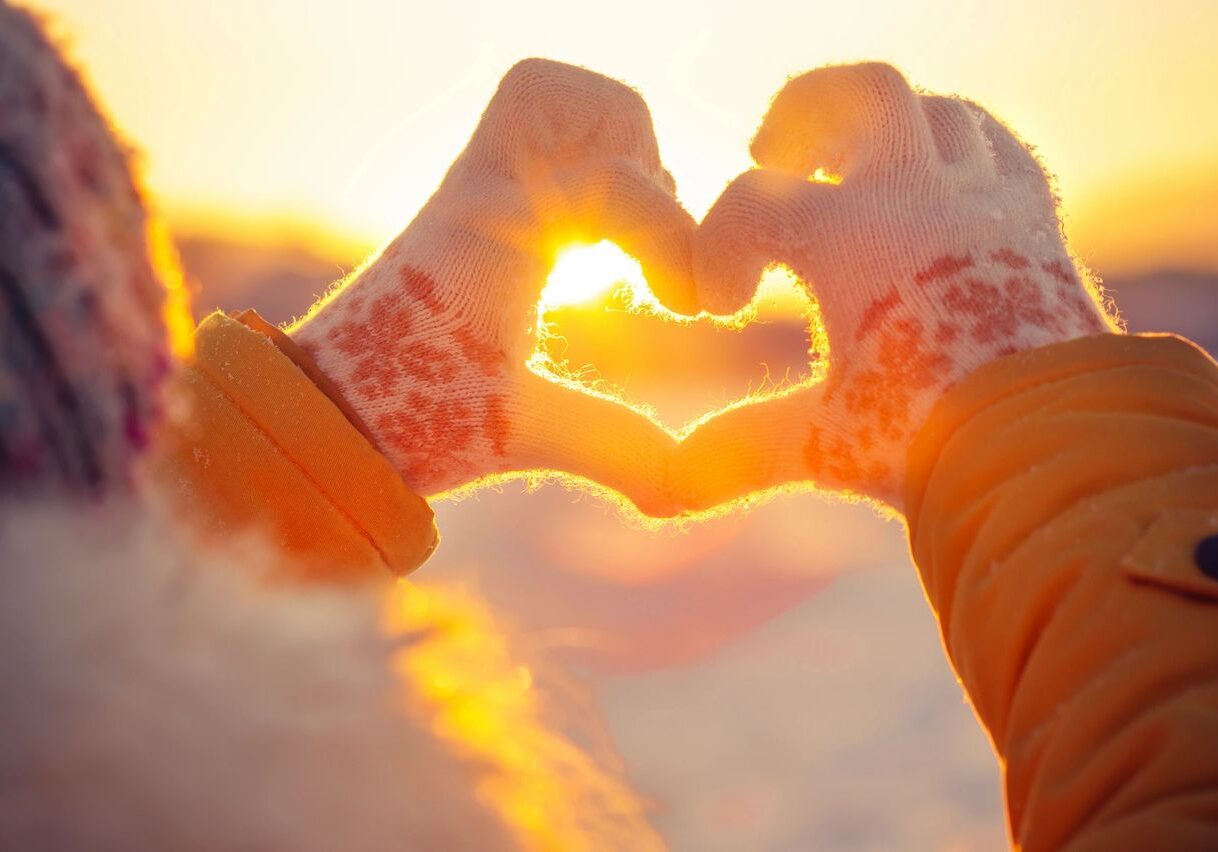 Gloved hands forming heart shape at sunset.