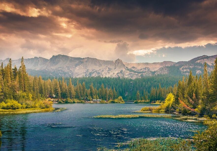 Mountain lake with trees and dramatic sky.